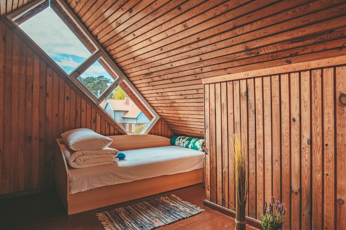 A cozy attic bedroom with a sloped ceiling, a bed with white linens, a view through a skylight, and a wooden wall.