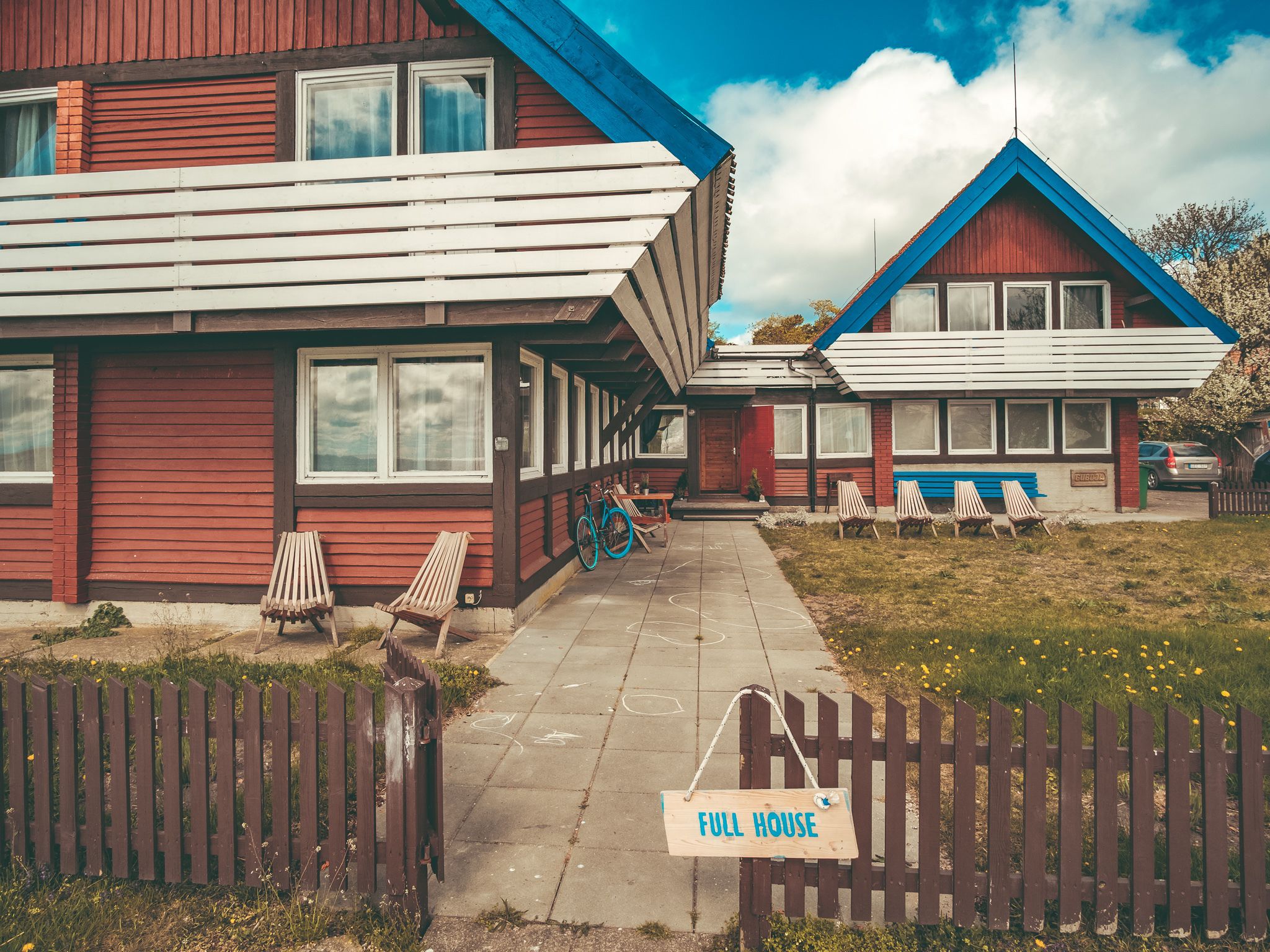 Une maison en bois avec une pancarte indiquant « COMPLET », un vélo et des sièges à l’extérieur.