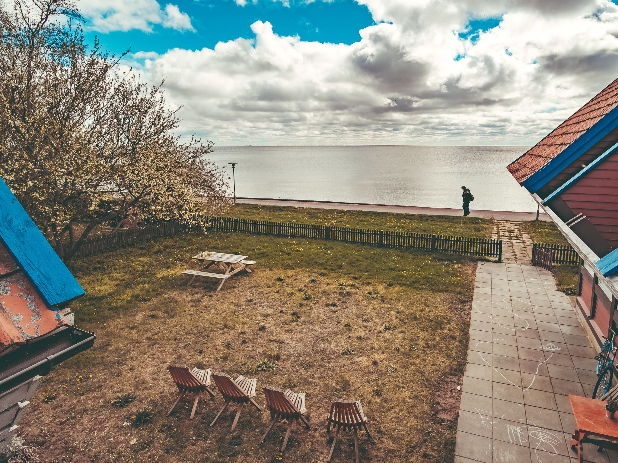 A grassy outdoor area with a picnic table and chairs, a wooden fence, and a view of the water.