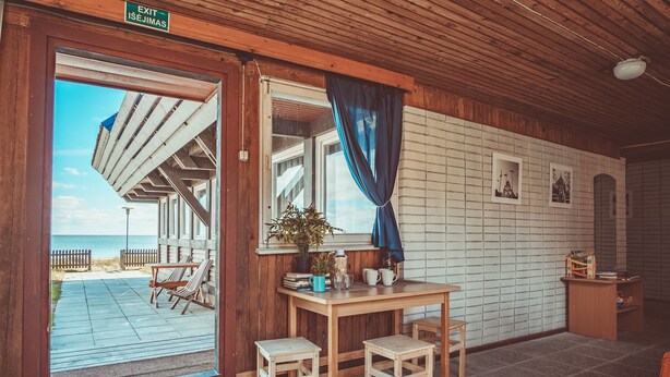 A wooden interior with a view of the beach, a table with chairs, and a small shelf with items. - Guboja (Neringa)