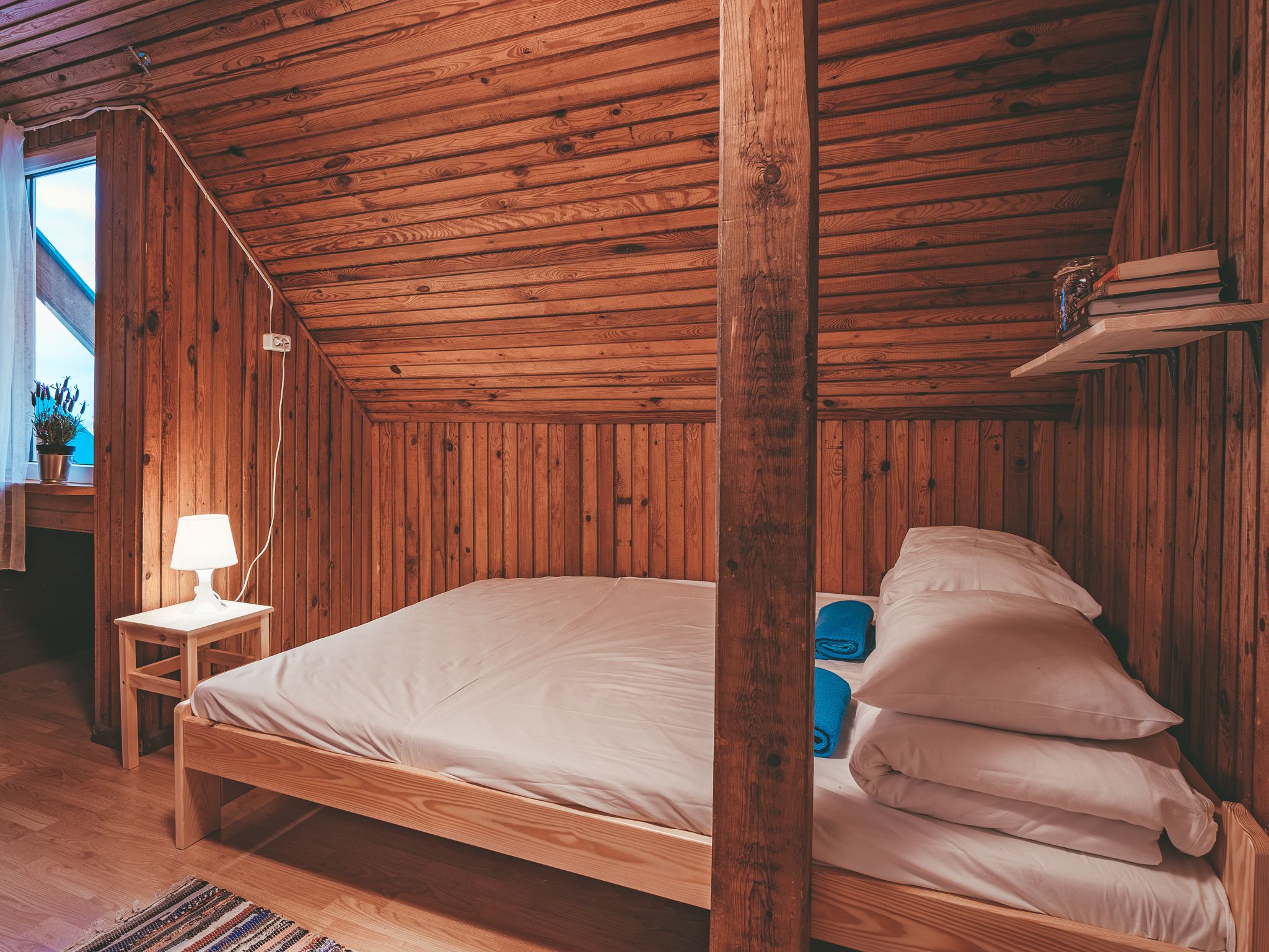 Une chambre dans une cabane en bois, avec un lit simple, une table de chevet avec une lampe et une étagère remplie de livres.