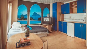 A modern room with a bed, a TV, a dining table with books, and a view of the sea through arched windows. - Guboja (Neringa)