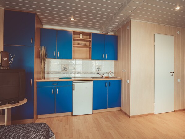 A compact kitchen with blue cabinets, a white countertop, and a wooden door. - Guboja (Neringa)