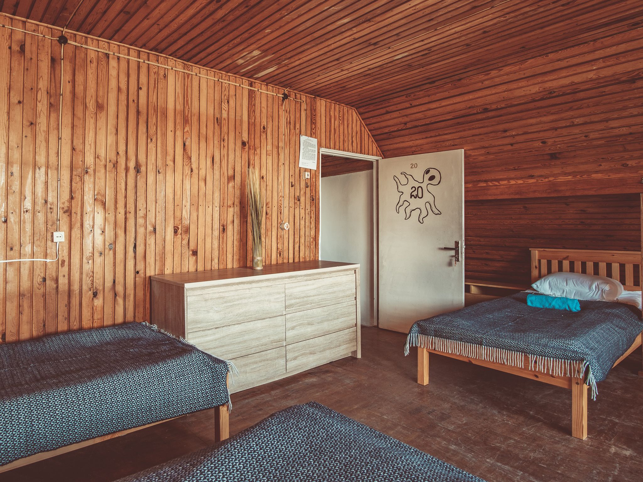 A wooden cabin room with two beds, a dresser, and a door with a number.