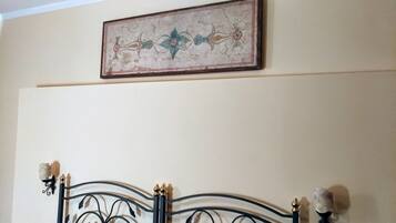 Een kamer met een bed met een zwart metalen frame en decoratieve details. Boven het bed hangt een kunstwerk met een bloemenmotief.