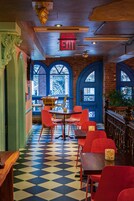 Een restaurantinterieur met een geruit vloertje, rode stoelen, een houten tafel en een bakstenen muur.