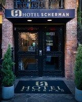 De ingang van Hotel Sherman, met een gevel van baksteen, dubbele deuren met ingewikkeld ijzerwerk en een deurmat met de naam van het hotel.