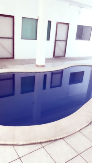 A swimming pool with a curved edge, surrounded by a tiled floor. - HOTEL SAN PATRICIO (San Patricio Melaque)