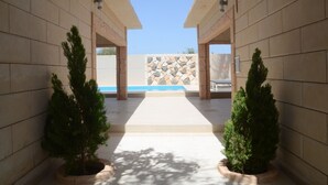 A corridor with tiled walls, potted evergreen trees, and a view of a pool area. - Appart Hôtel La Perle (St. Louis)