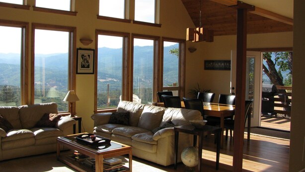 Ein großzügiger Wohnbereich mit einem großen Fenster mit Blick auf eine Berglandschaft, ein Essbereich mit Holztisch und -stühlen sowie eine gemütliche Sitzecke mit Sofa und Couchtisch.