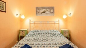 Un dormitorio con una cama, dos mesitas de noche, una mesilla auxiliar, un cuadro colgado en la pared y dos lámparas de pared.