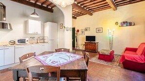 Un espacio de sala acogedor con una mesa de comedor de madera, sillas, un sofá rojo, un televisor y una estantería.