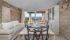 A cozy dining area with a table set for four, a sofa, and a view of the sea. - Villa Laura in Punta Tramontana - Castelsardo (CASTELSARDO)