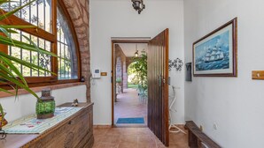 A hallway with a wooden bench, a decorative cabinet, a door leading to a garden, and a framed painting on the wall. - Villa Laura in Punta Tramontana - Castelsardo (CASTELSARDO)