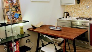 A compact kitchen with a wooden table, a chair, a corkboard with various items, and a tiled backsplash.