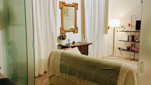 A bedroom with a bed, a bedside table, a mirror, a wardrobe, and a desk with a lamp.