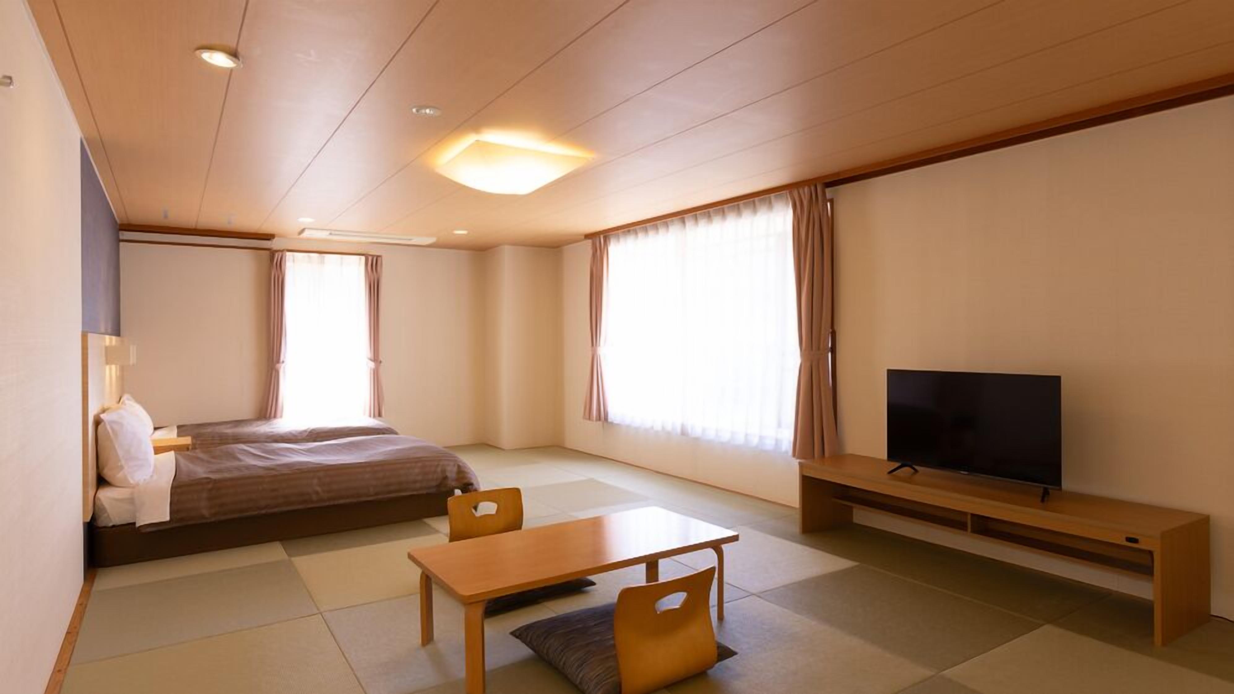 A hotel room with a bed, a TV, a table, and a chair.