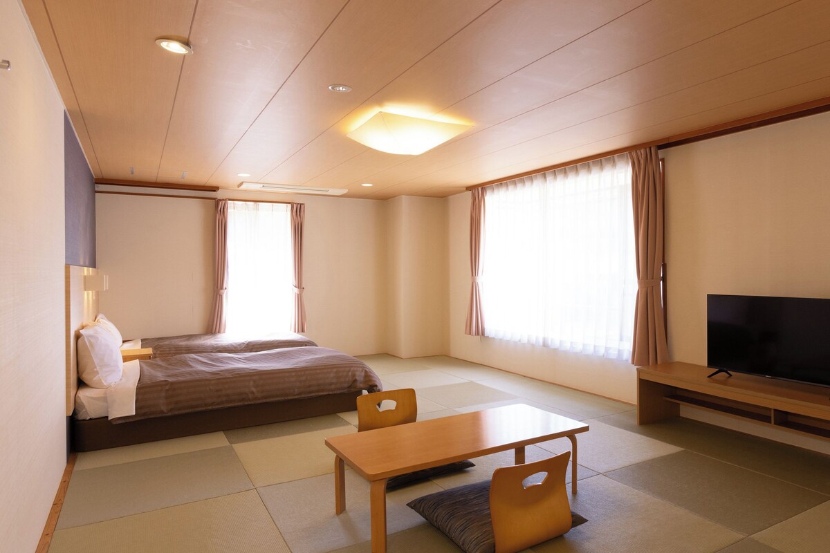 A hotel room with a bed, a TV, a table, and a chair.