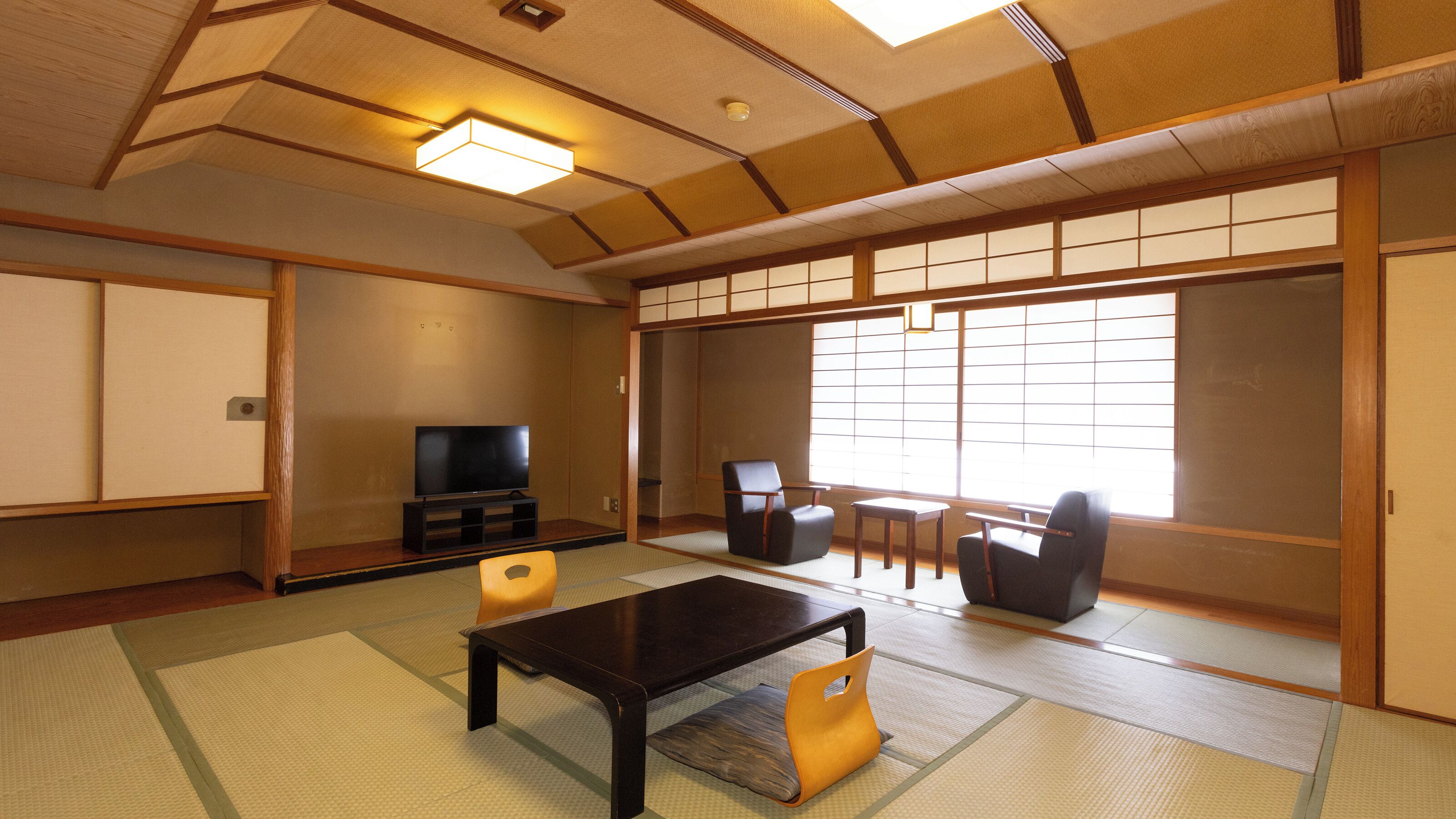 A traditional Japanese room with tatami flooring, a television, a low table, and sliding doors.