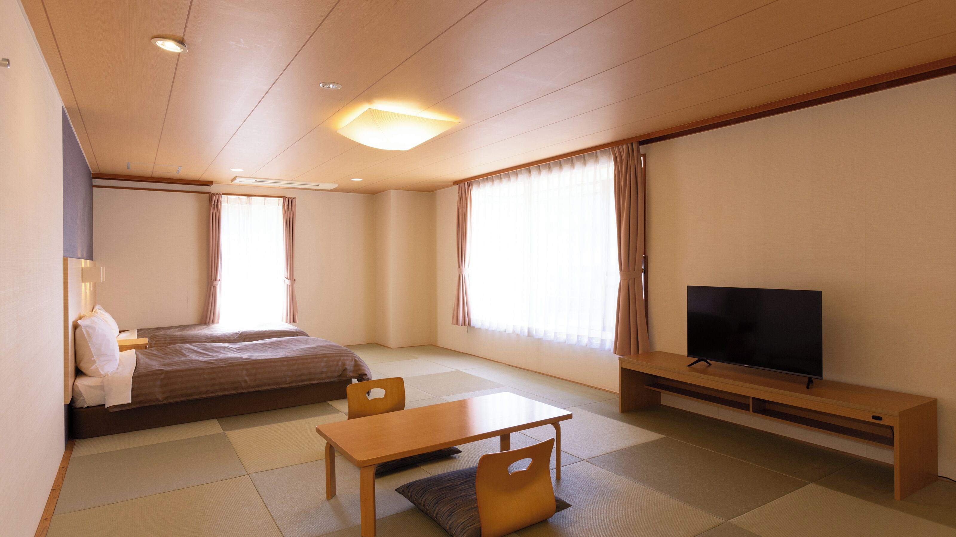 A hotel room with a bed, a TV, a table, and a chair.