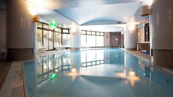 An indoor swimming pool with clear glass walls, a tiled floor, and a ceiling with a ribbed design.