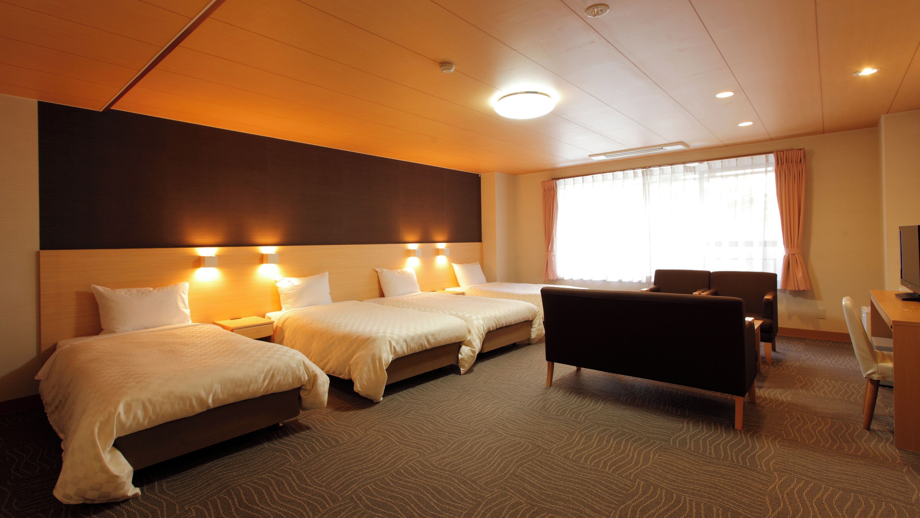 A hotel room with two beds, a desk, a chair, and a large window with curtains.