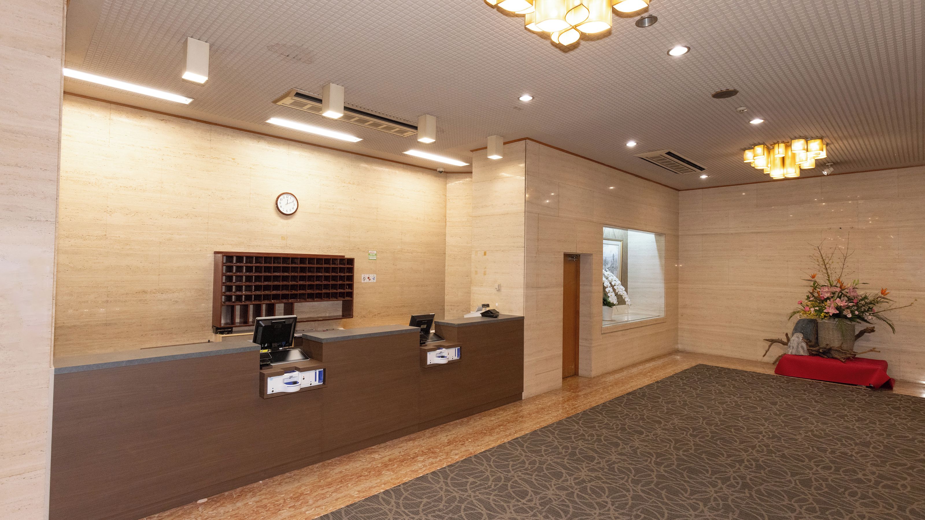 A reception area with a reception desk, a clock, a window, and a plant.