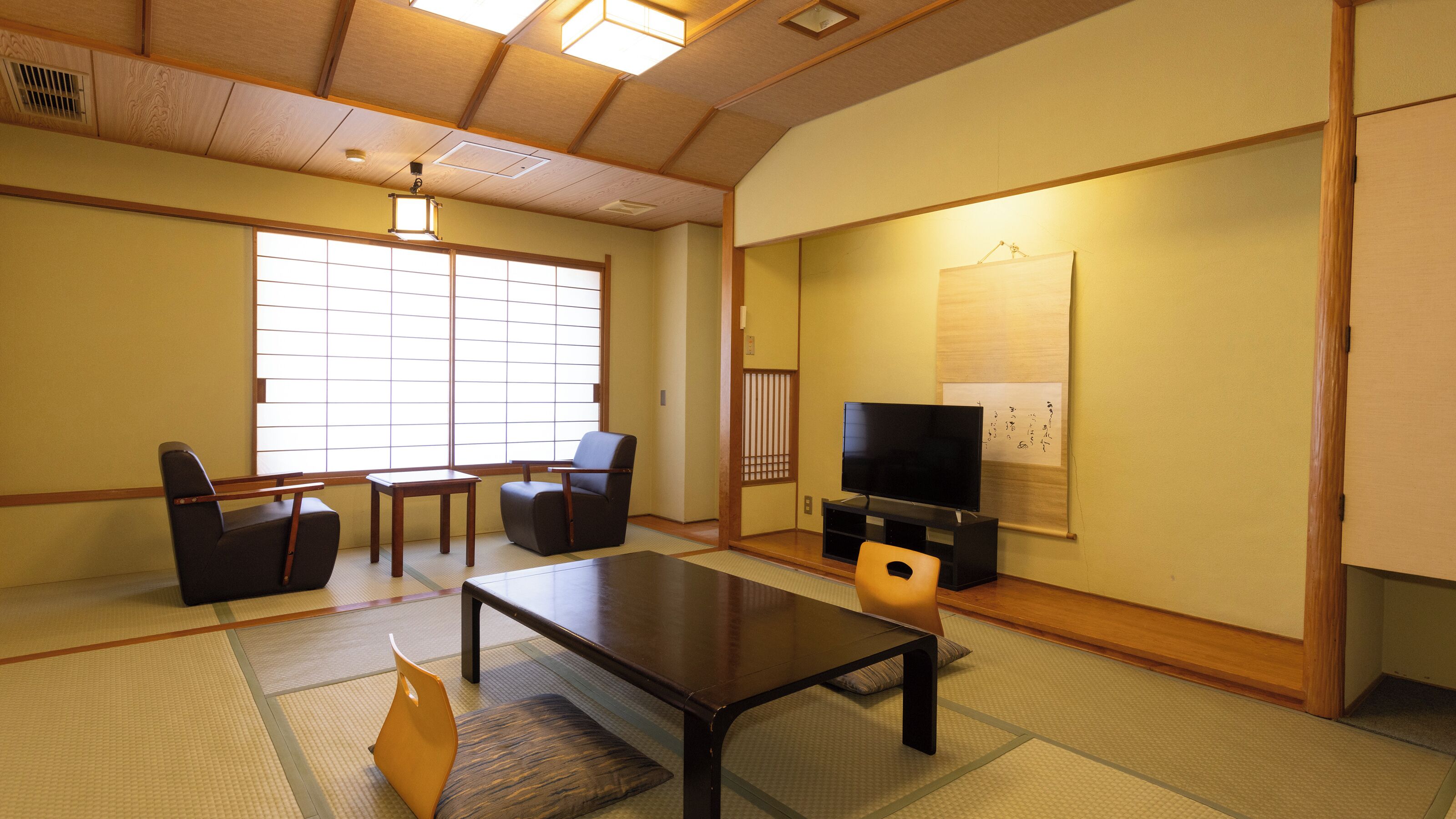 A traditional Japanese-style room with tatami flooring, a low table, two chairs, a television, and a shoji screen.