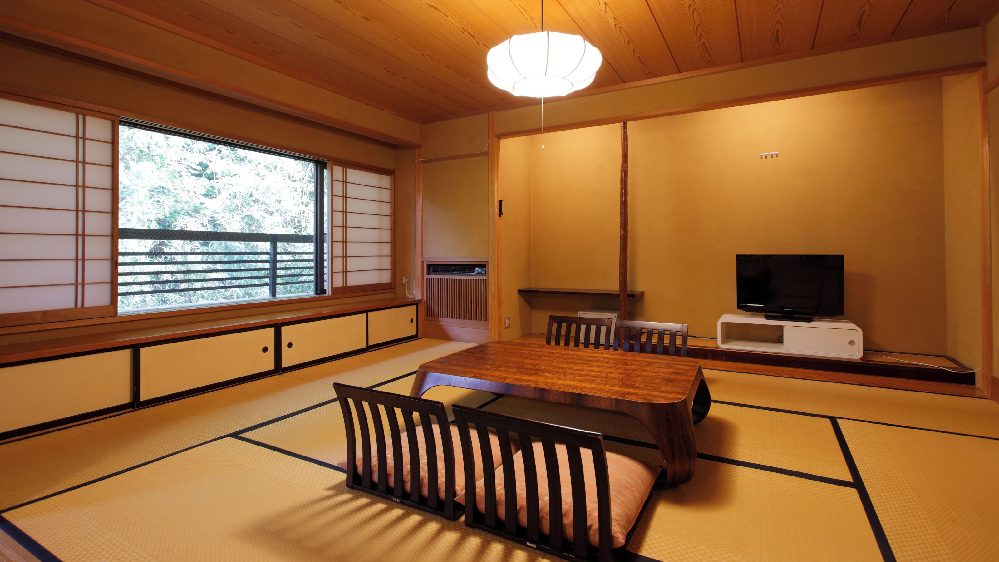 A traditional Japanese room with tatami flooring, a low table, a TV, and sliding doors.