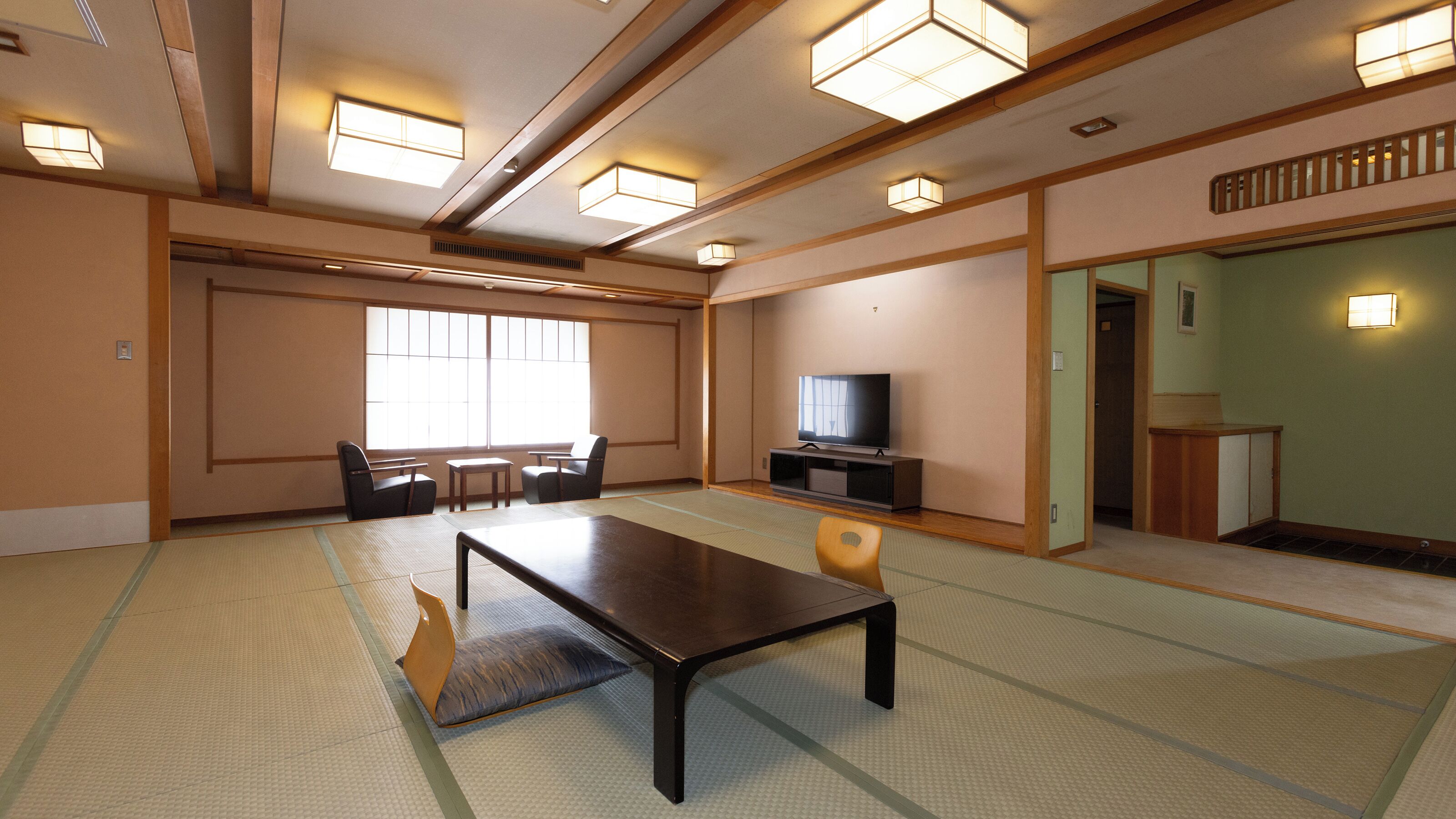 A traditional Japanese-style room with tatami flooring, a low table, chairs, a television, and sliding doors.