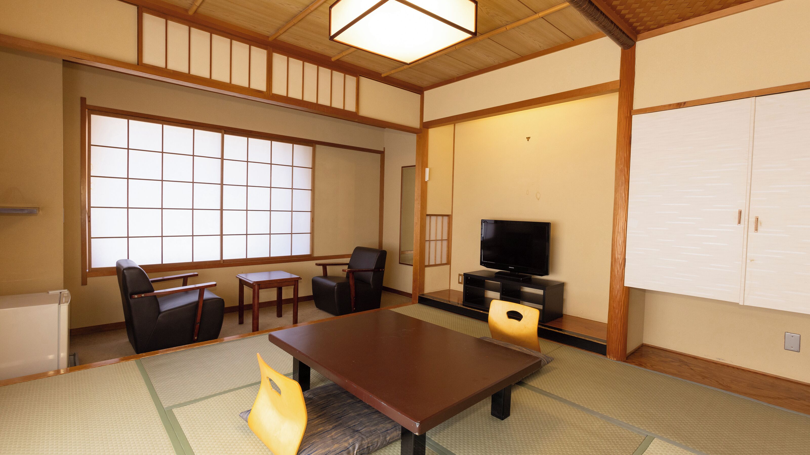 A traditional Japanese-style room with tatami flooring, a television, a cabinet, and sliding doors.