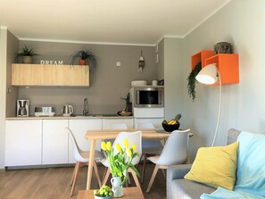 Une cuisine moderne avec des meubles blancs, un four à micro-ondes et une machine à café. On y trouve également un coin repas avec une table, des chaises et un vase rempli de fleurs jaunes.