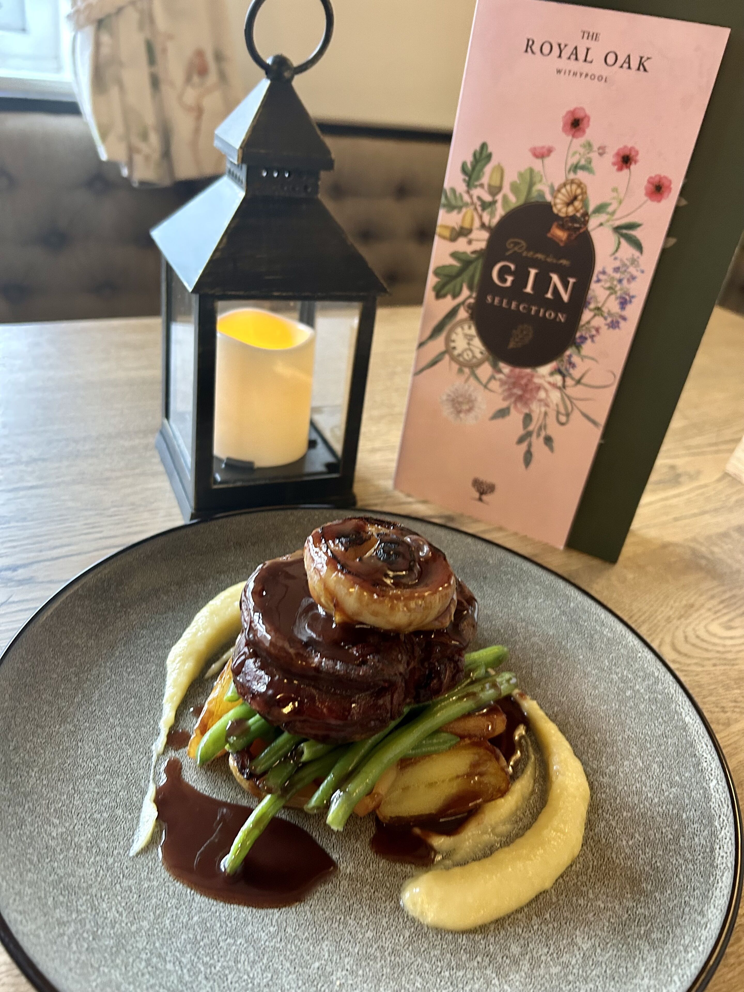 A plate of food with a candle and a book titled "The Royal Oak Gin Collection" in the background.