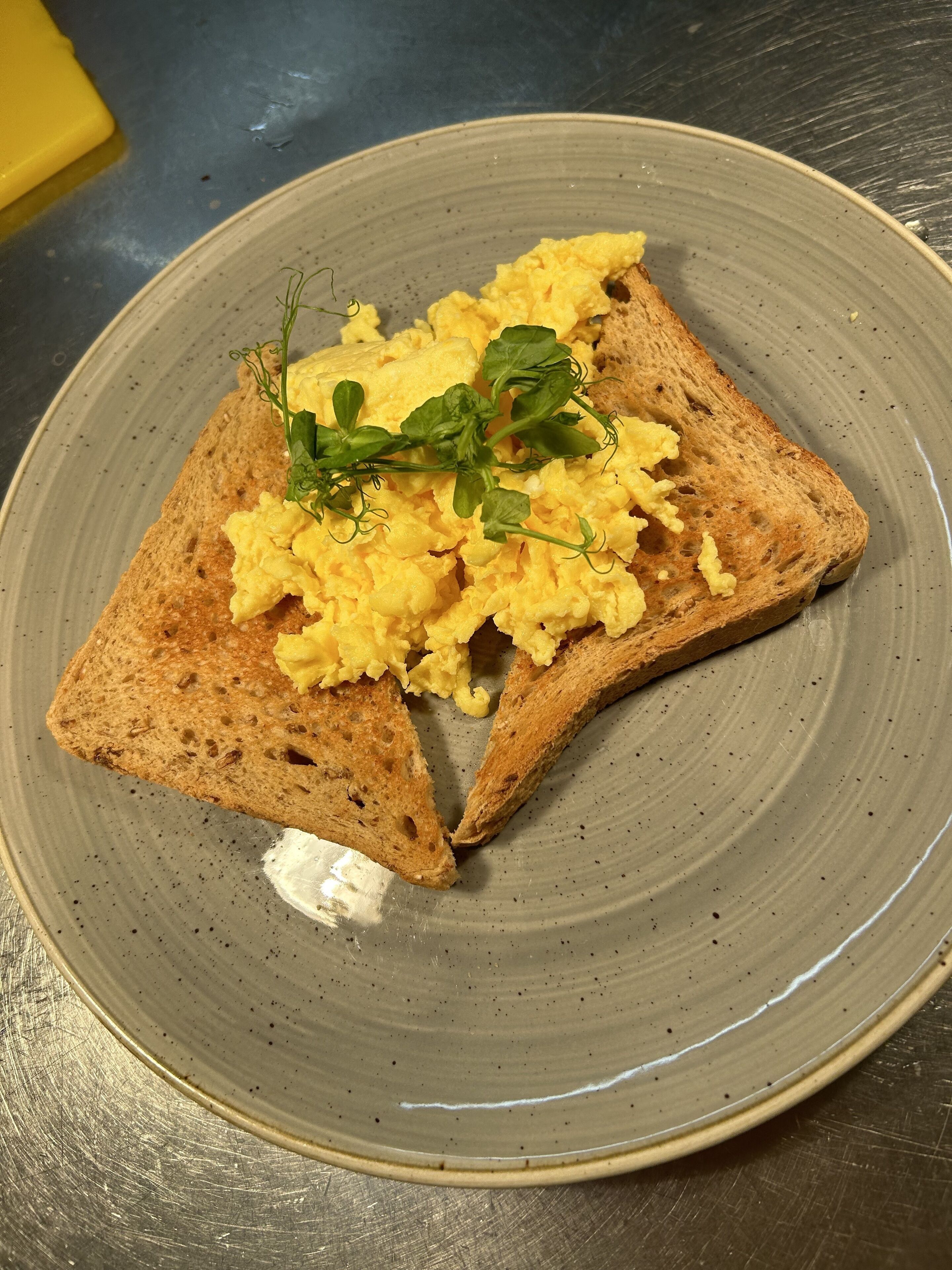 Un plato con huevos revueltos y una ramita de verdura sobre un plato de cerámica.