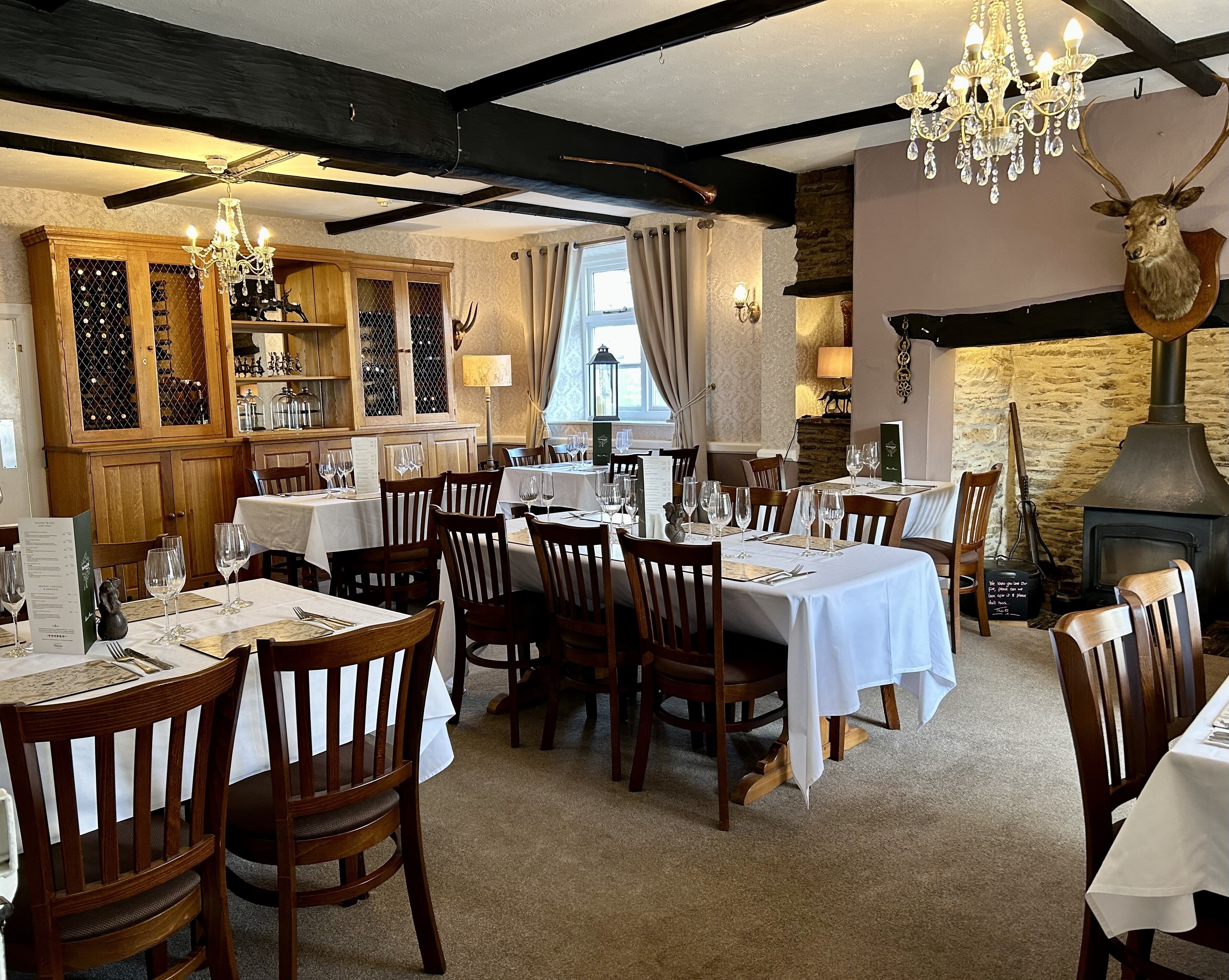A restaurant with wooden tables and chairs, chandeliers, and a stone fireplace.