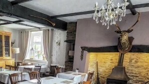 Un comedor con mesas redondas, sillas de madera, una araña y una chimenea de piedra.