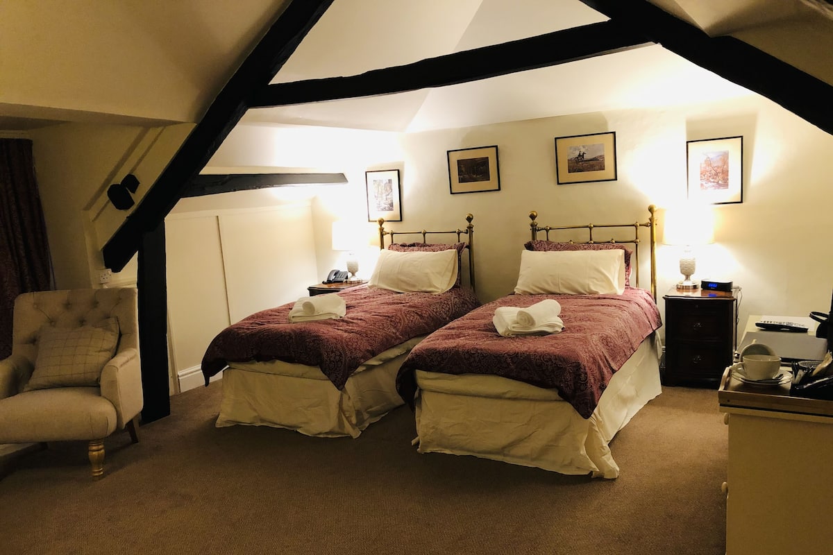 A room with two beds, a chair, a desk, and a lamp.