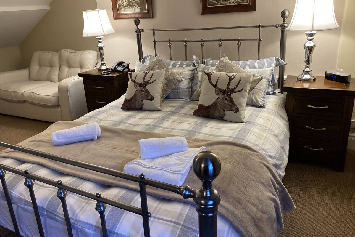 A bedroom with a bed, a nightstand, a lamp, a chair, and two framed pictures on the wall.