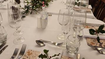 Mesa de comedor dispuesta con varias copas de vino, cubiertos y elementos decorativos como acebo y un florero.