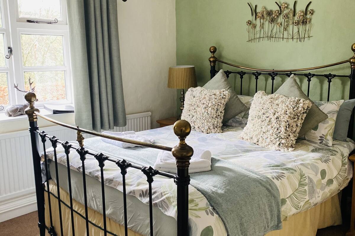 A neatly made bed with a floral bedspread, a bedside lamp, and a window with curtains.