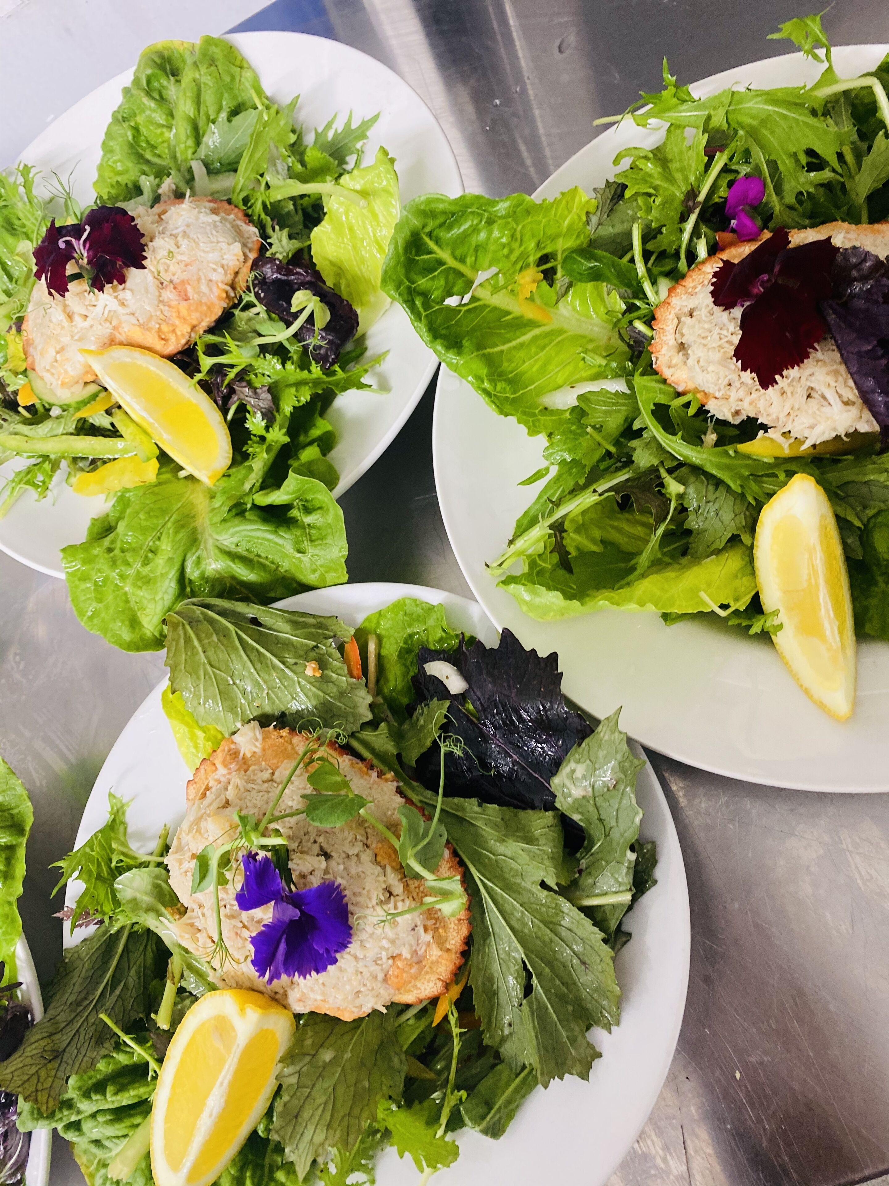 Three plates of salad with various greens and lemon slices.
