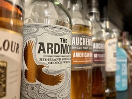 Una fila de botellas de whisky con etiquetas, incluyendo 'The Ardmo Highland Single Malt Scotch Whisky'.