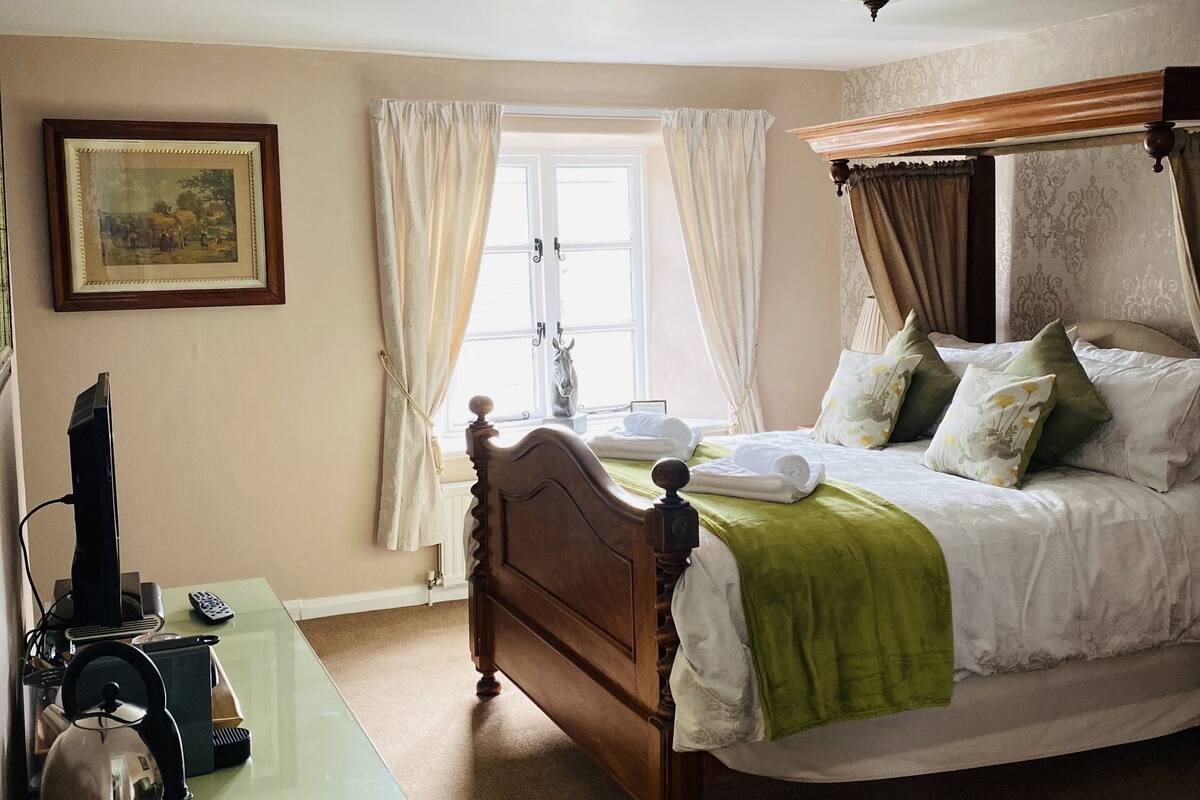 A bedroom with a wooden bed, a desk with a computer, a chair, and a window with curtains.