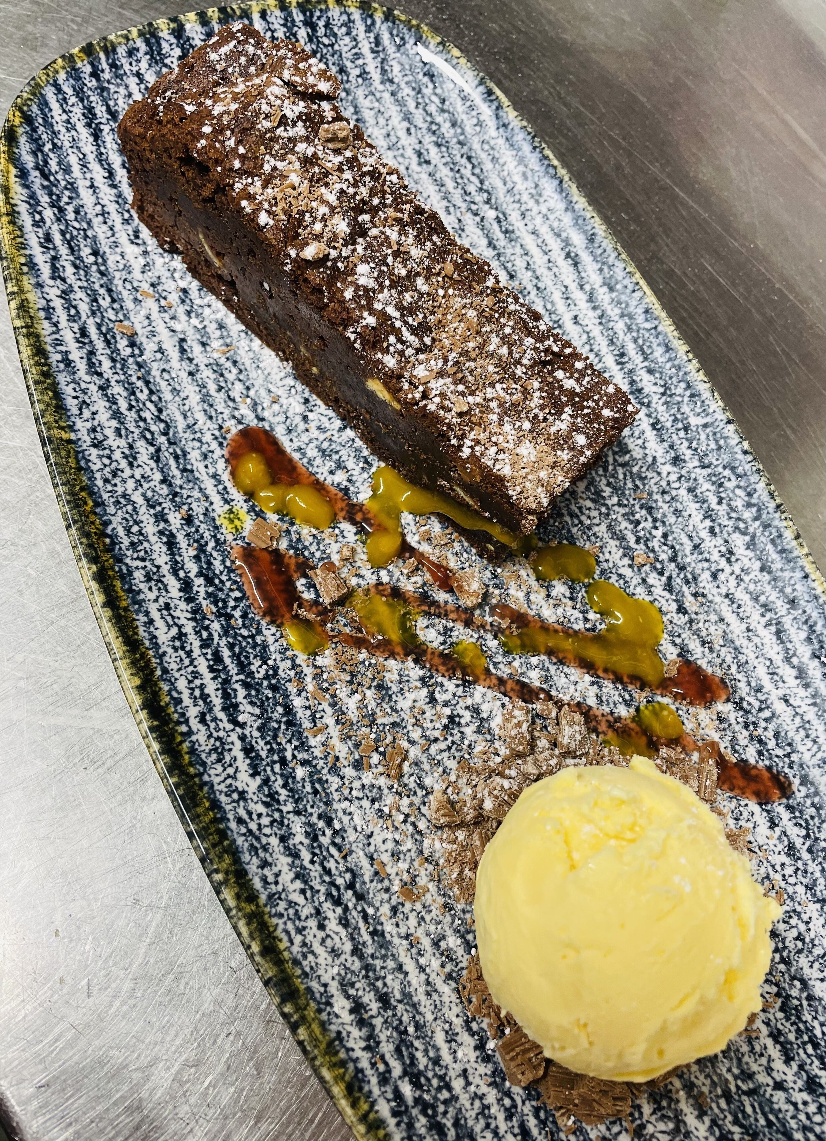 A dessert plate with a brownie, caramel sauce, and a scoop of vanilla ice cream.