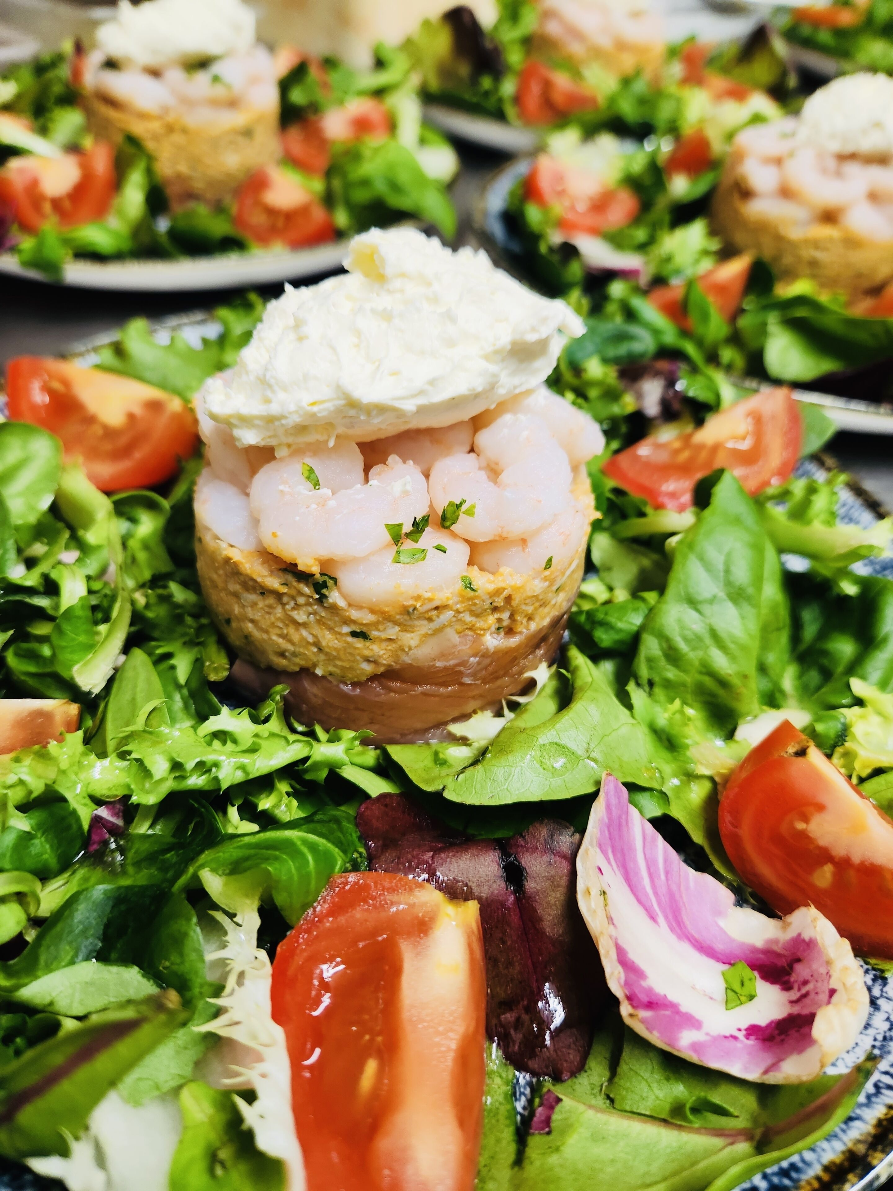 Salada com camarão sobre uma base de pão, cercada por diversas folhas verdes e tomates.