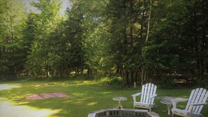 A circular fire pit with seating around it, surrounded by a grassy area and trees.
