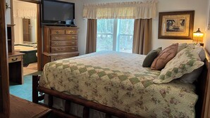 A bedroom with a bed, dresser, television, and a window with curtains.