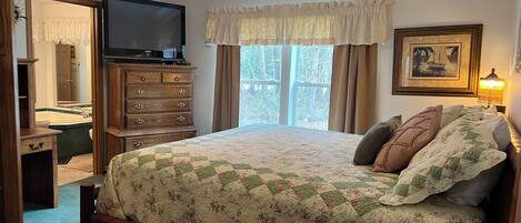 Un dormitorio con cama, cómoda, televisor y ventana con cortinas.