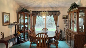 A dining room with a wooden table and chairs, a chandelier, and two wooden cabinets with glass doors.
