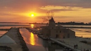 Un moulin à vent traditionnel et un canal où naviguent des bateaux, le tout baigné par les couleurs du coucher de soleil.